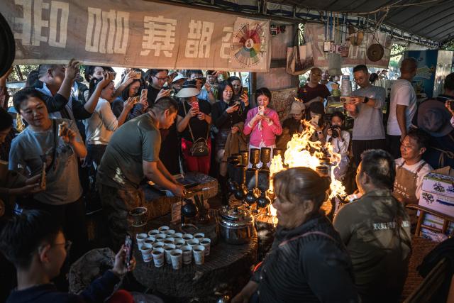(251214) -- KUNMING, Dec. 14, 2025 (Xinhua) -- Customers shoot the process of making coffee at a cafe run by Li Jinhe in Mangkuan Township of Baoshan City, southwest China's Yunnan Province, Nov. 15, 2025.
  Mandabatmaz, a Turkish cafe, is located in a small alley beside Istiklal Avenue in Istanbul.
  The owner, Can Ozmen, took over this small coffee shop with a history of nearly sixty years from his parents. To carry on the tradition, he still insists on brewing coffee with copper pots. Ozmen introduced that Turkish coffee should be consumed with coffee grounds, which makes Turkish coffee unique. "Unlike other coffees, which are filtered, Turkish coffee is enjoyed in its entirety," Ozmen explained.
  Turkish coffee has a long history and was inscribed on UNESCO's Representative List of the Intangible Cultural Heritage of Humanity in 2013.
  While in China, a riverside cafe in Yunnan also wins fame among coffee lovers.
  Li Jinhe, 53, has operated his cafe in Mangkuan under Baoshan City in Gaoligong Mountains for 14 years.
  His "flame-brewed coffee", which made by a blowtorch to heat beneath siphon pots, has taken the Internet by storm for its originality, turning his cafe into a viral sensation.
  Tourists said that the coffee shop by the Nujiang River has broken the stereotype of urban coffee, and coffee should be a daily drink integrated into life.
  "I grew up here, and love Gaoligong Mountains," said Li. The Gaoligong Mountains, where fertile soil, ideal temperatures and abundant sunlight situate it within the global coffee-growing belt, boast small-bean coffee. "It is my unwavering commitment to promote local small-bean coffee," added Li.
  Although made by different ways, both Turkish and Chinese coffee tell the story of people's pursuit of life with warmth and aroma. (Xinhua/Wang Guansen)