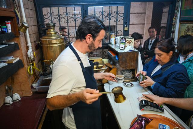 (251214) -- ISTANBUL, Dec. 14, 2025 (Xinhua) -- Can Ozmen (L), owner of the Turkish cafe Mandabatmaz, communicates with a customer while preparing coffee at the cafe in Istanbul, Türkiye, Nov. 22, 2025.
  Mandabatmaz, a Turkish cafe, is located in a small alley beside Istiklal Avenue in Istanbul.
  The owner, Can Ozmen, took over this small coffee shop with a history of nearly sixty years from his parents. To carry on the tradition, he still insists on brewing coffee with copper pots. Ozmen introduced that Turkish coffee should be consumed with coffee grounds, which makes Turkish coffee unique. "Unlike other coffees, which are filtered, Turkish coffee is enjoyed in its entirety," Ozmen explained.
  Turkish coffee has a long history and was inscribed on UNESCO's Representative List of the Intangible Cultural Heritage of Humanity in 2013.
  While in China, a riverside cafe in Yunnan also wins fame among coffee lovers.
  Li Jinhe, 53, has operated his cafe in Mangkuan under Baoshan City in Gaoligong Mountains for 14 years.
  His "flame-brewed coffee", which made by a blowtorch to heat beneath siphon pots, has taken the Internet by storm for its originality, turning his cafe into a viral sensation.
  Tourists said that the coffee shop by the Nujiang River has broken the stereotype of urban coffee, and coffee should be a daily drink integrated into life.
  "I grew up here, and love Gaoligong Mountains," said Li. The Gaoligong Mountains, where fertile soil, ideal temperatures and abundant sunlight situate it within the global coffee-growing belt, boast small-bean coffee. "It is my unwavering commitment to promote local small-bean coffee," added Li.
  Although made by different ways, both Turkish and Chinese coffee tell the story of people's pursuit of life with warmth and aroma. (Xinhua/Liu Lei)