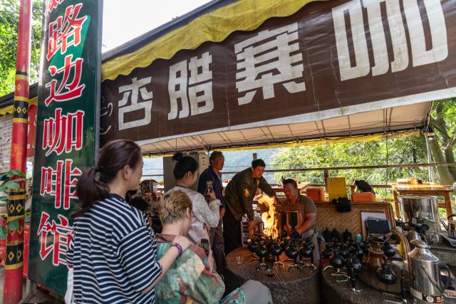 (251214) -- KUNMING, Dec. 14, 2025 (Xinhua) -- People watch Li Jinhe (R) making coffee at his cafe in Mangkuan Township of Baoshan City, southwest China's Yunnan Province, Nov. 15, 2025.
  Mandabatmaz, a Turkish cafe, is located in a small alley beside Istiklal Avenue in Istanbul.
  The owner, Can Ozmen, took over this small coffee shop with a history of nearly sixty years from his parents. To carry on the tradition, he still insists on brewing coffee with copper pots. Ozmen introduced that Turkish coffee should be consumed with coffee grounds, which makes Turkish coffee unique. "Unlike other coffees, which are filtered, Turkish coffee is enjoyed in its entirety," Ozmen explained.
  Turkish coffee has a long history and was inscribed on UNESCO's Representative List of the Intangible Cultural Heritage of Humanity in 2013.
  While in China, a riverside cafe in Yunnan also wins fame among coffee lovers.
  Li Jinhe, 53, has operated his cafe in Mangkuan under Baoshan City in Gaoligong Mountains for 14 years.
  His "flame-brewed coffee", which made by a blowtorch to heat beneath siphon pots, has taken the Internet by storm for its originality, turning his cafe into a viral sensation.
  Tourists said that the coffee shop by the Nujiang River has broken the stereotype of urban coffee, and coffee should be a daily drink integrated into life.
  "I grew up here, and love Gaoligong Mountains," said Li. The Gaoligong Mountains, where fertile soil, ideal temperatures and abundant sunlight situate it within the global coffee-growing belt, boast small-bean coffee. "It is my unwavering commitment to promote local small-bean coffee," added Li.
  Although made by different ways, both Turkish and Chinese coffee tell the story of people's pursuit of life with warmth and aroma. (Xinhua/Gao Yongwei)