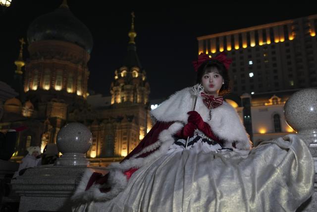 (251215) -- HARBIN, Dec. 15, 2025 (Xinhua) -- A tourist in costume poses for a photo at a square of architecture art in Harbin, northeast China's Heilongjiang Province, Dec. 15, 2025. The square, where the landmark St. Sophia Cathedral, a former Russian Orthodox church and a perfect example of Neo-Byzantine architectures, is located, has become a hot spot for tourists to take travel photos. (Xinhua/Wang Song)