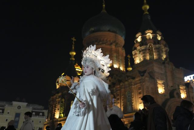 (251216) -- BEIJING, Dec. 16, 2025 (Xinhua) -- A tourist in costume poses for a photo at a square of architecture art in Harbin, northeast China's Heilongjiang Province, Dec. 15, 2025. The square, where the landmark St. Sophia Cathedral, a former Russian Orthodox church, is located, has become a hot spot for tourists to take travel photos. (Xinhua/Wang Song)