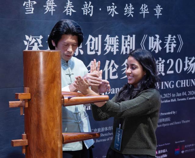 (251216) -- TORONTO, Dec. 16, 2025 (Xinhua) -- A guest (R) experiences Wing Chun with a wooden dummy during a media day event in Toronto, Canada, on Dec. 15, 2025. The Chinese dance drama will be staged here from Dec. 16, 2025 to Jan. 4, 2026. (Photo by Zou Zheng/Xinhua)