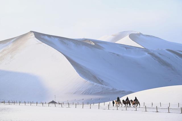 (251216) -- BEIJING, Dec. 16, 2025 (Xinhua) -- Tourists ride camels to enjoy the snowy scenery at the Mingsha Mountain and Crescent Spring Scenic Area in Dunhuang City, northwest China's Gansu Province, Dec. 12, 2025. (Photo by Zhang Xiaoliang/Xinhua)