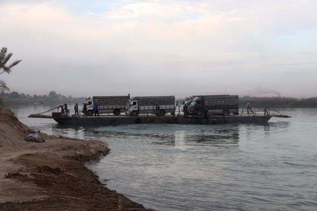 (251216) -- DEIR AL-ZOUR, Dec. 16, 2025 (Xinhua) -- Trucks loaded with goods are seen aboard a flat-bottomed ferry crossing the Euphrates River in Deir al-Zour province, eastern Syria, Dec. 12, 2025. TO GO WITH "Feature: Ferries of fear -- war-weary Syrians forced to risk lives on the Euphrates" (Str/Xinhua)