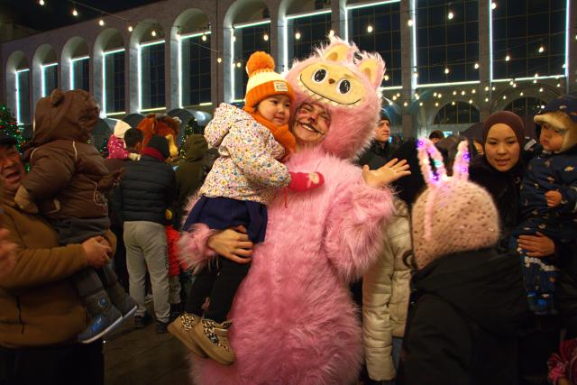 (251216) -- BISHKEK, Dec. 16, 2025 (Xinhua) -- People interact with a Labubu mascot, a popular furry doll from Chinese toy company Pop Mart, during the New Year tree lighting ceremony in Bishkek, Kyrgyzstan, Dec. 15, 2025. (Photo by Liu Xiaowan/Xinhua)