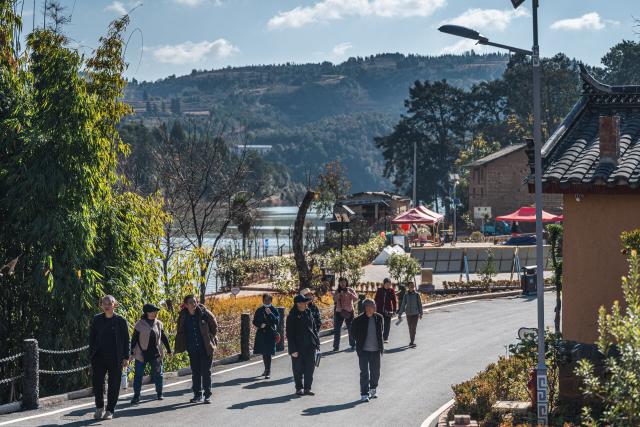 (251216) -- QUJING, Dec. 16, 2025 (Xinhua) -- Tourists take a walk in the Huangba neighborhood of Qujing City, southwest China's Yunnan Province, Dec. 16, 2025. The Huangba neighborhood is one of the local model travel destinations promoted by Qujing City, which has in recent years made great efforts to help transform the local ecological advantages into tourism resources. A number of livable and business-friendly villages are built here for rural revitalization. (Xinhua/Wang Guansen)