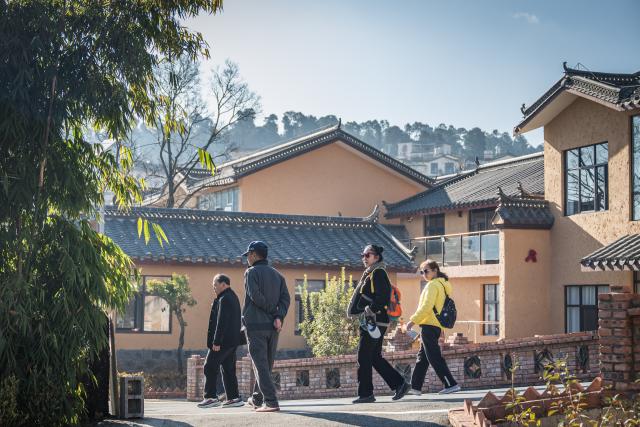 (251216) -- QUJING, Dec. 16, 2025 (Xinhua) -- Tourists take a walk in the Huangba neighborhood of Qujing City, southwest China's Yunnan Province, Dec. 16, 2025. The Huangba neighborhood is one of the local model travel destinations promoted by Qujing City, which has in recent years made great efforts to help transform the local ecological advantages into tourism resources. A number of livable and business-friendly villages are built here for rural revitalization. (Xinhua/Wang Guansen)