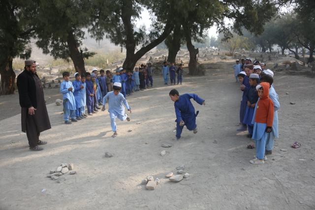(251217) -- NANGARHAR, Dec. 17, 2025 (Xinhua) -- Students take part in traditional games at a makeshift roadside school without proper shelters beside a highway junction in Nangarhar province, eastern Afghanistan, Dec. 16, 2025. (Photo by Saifurahman Safi/Xinhua)