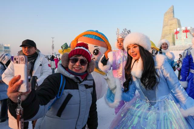 (251217) -- HARBIN, Dec. 17, 2025 (Xinhua) -- A tourist takes selfies with a parading performer at the Harbin Ice-Snow World in Harbin, northeast China's Heilongjiang Province, Dec. 17, 2025. The Harbin Ice-Snow World, world's largest ice and snow theme park, officially opened for the season on Wednesday, unveiling its most spectacular edition yet, featuring landmark attractions, thoughtful services and magnificent ice sculptures across a record 1.2 million square meters of park area. (Xinhua/Wang Jianwei)