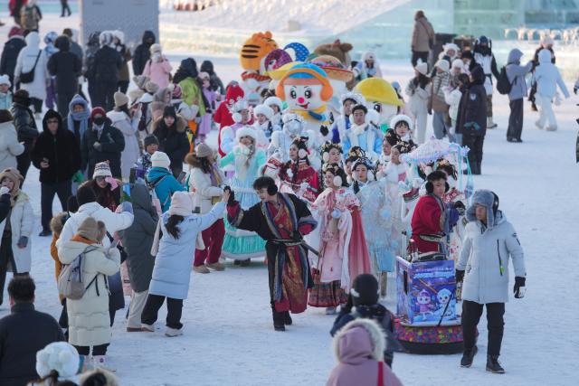 (251217) -- HARBIN, Dec. 17, 2025 (Xinhua) -- Tourists interact with parading performers at the Harbin Ice-Snow World in Harbin, northeast China's Heilongjiang Province, Dec. 17, 2025. The Harbin Ice-Snow World, world's largest ice and snow theme park, officially opened for the season on Wednesday, unveiling its most spectacular edition yet, featuring landmark attractions, thoughtful services and magnificent ice sculptures across a record 1.2 million square meters of park area. (Xinhua/Wang Jianwei)