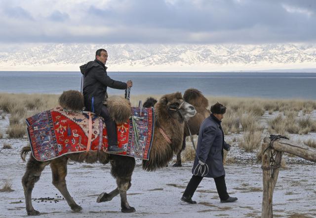 (251217) -- URUMQI, Dec. 17, 2025 (Xinhua) -- A herdsman (L) riding a camel is seen by the Sayram Lake in Bortala Mongolian Autonomous Prefecture, northwest China's Xinjiang Uygur Autonomous Region, Dec. 15, 2025. (Xinhua/Wang Fei)