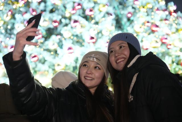 (251220) -- ASTANA, Dec. 20, 2025 (Xinhua) -- People take selfies as a New Year tree is lit up in Astana, Kazakhstan, Dec. 19, 2025. A New Year tree lighting ceremony was held in Astana on Friday, with more than 40 large New Year trees lit up across the city. The ceremony was accompanied by a citywide "fairy-tale fest" featuring concerts, dance performances and fireworks. (Photo by Kalizhan Ospanov/Xinhua)
