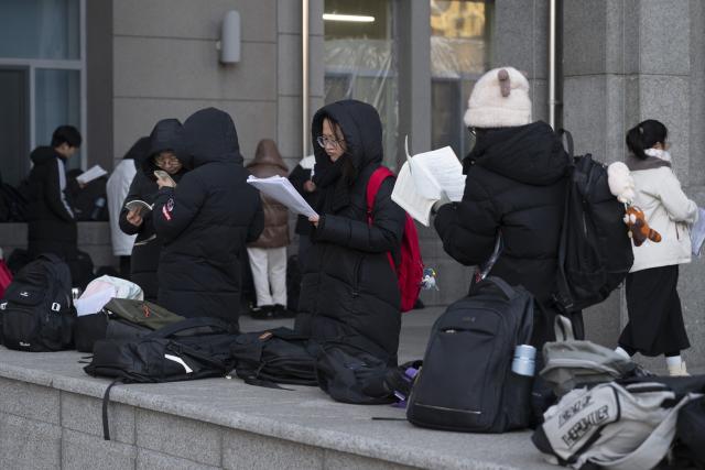 (251220) -- BEIJING, Dec. 20, 2025 (Xinhua) -- Examinees review their study materials outside an examination site for the 2026 postgraduate entrance exam in Harbin, northeast China's Heilongjiang Province, Dec. 20, 2025. China's national exam for postgraduate enrolment kicked off on Saturday. (Xinhua/Zhang Tao)