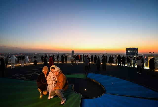 (251221) -- TIANJIN, Dec. 21, 2025 (Xinhua) -- Visitors pose for photos at the Jinwan Yunding sightseeing deck in Heping District of Tianjin, north China on Dec. 20, 2025. Recently, the Jinwan Yunding sightseeing deck, located at the Jinwan Plaza in Heping District of Tianjin, has begun operation. Visitors can ascend to the 300-meter-high rooftop to overlook Tianjin's urban view. (Xinhua/Zhao Zishuo)