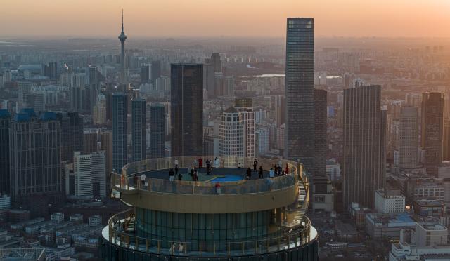 (251221) -- TIANJIN, Dec. 21, 2025 (Xinhua) -- An aerial drone photo taken on Dec. 20, 2025 shows visitors enjoying the urban view at sunset at the Jinwan Yunding sightseeing deck in Heping District of Tianjin, north China. Recently, the Jinwan Yunding sightseeing deck, located at the Jinwan Plaza in Heping District of Tianjin, has begun operation. Visitors can ascend to the 300-meter-high rooftop to overlook Tianjin's urban view. (Xinhua/Zhao Zishuo)