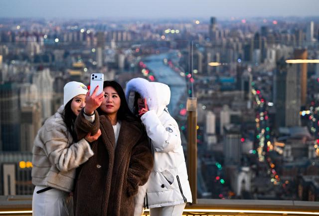 (251221) -- TIANJIN, Dec. 21, 2025 (Xinhua) -- Visitors pose for a selfie at the Jinwan Yunding sightseeing deck in Heping District of Tianjin, north China on Dec. 20, 2025. Recently, the Jinwan Yunding sightseeing deck, located at the Jinwan Plaza in Heping District of Tianjin, has begun operation. Visitors can ascend to the 300-meter-high rooftop to overlook Tianjin's urban view. (Xinhua/Zhao Zishuo)