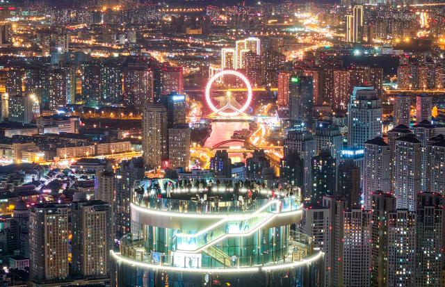 (251221) -- TIANJIN, Dec. 21, 2025 (Xinhua) -- An aerial drone photo taken on Dec. 20, 2025 shows visitors enjoying the night urban view at the Jinwan Yunding sightseeing deck in Heping District of Tianjin, north China. Recently, the Jinwan Yunding sightseeing deck, located at the Jinwan Plaza in Heping District of Tianjin, has begun operation. Visitors can ascend to the 300-meter-high rooftop to overlook Tianjin's urban view. (Xinhua)
