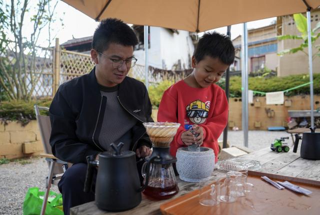 (251221) -- MOJIANG, Dec. 21, 2025 (Xinhua) -- A father with his son experiences making handmade coffee in Manhai Village, Mojiang Hani Autonomous County of Pu'er City, southwest China's Yunnan Province, Dec. 20, 2025. Manhai Village, located in Mojiang Hani Autonomous County of Pu'er City, is home to people from various ethnic groups. In recent years, with the help of the local government, the village has made significant strides in rural revitalization. 
  Manhai has converted idle houses into homestays and study tour centers. The village has also leveraged its intangible cultural heritage, such as bamboo weaving, to develop study tour classes and cultural and creative products. Furthermore, Manhai has trained villagers to run homestays and act as instructors during study tours. 
  Nowadays, the village has attracted many tourists and entrepreneurs to visit and start businesses. (Xinhua/Chen Xinbo)