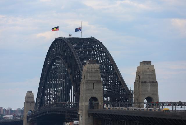 (251221) -- SYDNEY, Dec. 21, 2025 (Xinhua) -- Flags fly at half-mast on the Harbour Bridge to honor the victims of the deadly terror attack at Bondi Beach a week earlier in Sydney, Australia, Dec. 21, 2025, the National Day of Reflection. (Xinhua/Ma Ping)