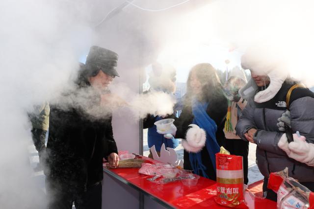 (251221) -- MOHE, Dec. 21, 2025 (Xinhua) -- People try local foods at a cultural festival on the occasion of the Winter Solstice in Beiji Village of Mohe City, northeast China's Heilongjiang Province, Dec. 21, 2025. People attended a cultural festival marking the Winter Solstice, the shortest day of the year, here on Sunday. (Photo by Shao Tianli/Xinhua)