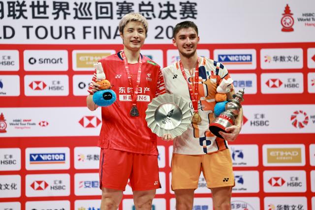 (251221) -- HANGZHOU, Dec. 21, 2025 (Xinhua) -- Winner Christo Popov (R) of France and Runner-up Shi Yuqi of China pose during the awarding ceremony for the men's singles final at BWF World Tour Finals 2025 in Hangzhou, east China's Zhejiang Province, Dec. 21, 2025. (Xinhua/Jiang Han)