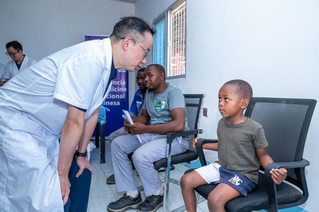 (251222) -- MAPUTO, Dec. 22, 2025 (Xinhua) -- A member of the 26th Chinese medical team to Mozambique talks to a boy during a free medical outreach in Maputo, Mozambique, Dec. 20, 2025. The 26th Chinese medical team conducted a free health outreach on Saturday for workers at an industrial company in Maputo, Mozambique's capital, providing on-site medical examinations that were widely praised by employees and company management. (Photo by Mendes Mondlane/Xinhua)