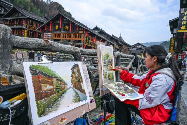(251223) -- LIPING, Dec. 23, 2025 (Xinhua) -- A student works on a painting in Zhaoxing Dong village of Liping County, southwest China's Guizhou Province, Dec. 19, 2025.
  Zhaoxing Dong village, home to a captivating cultural landscape, has seen an influx of tourists as the Dong New Year approaches.
  In recent years, the local government has leveraged the village's rich Dong ethnic cultural resources in developing the tourism industry.
  Boosted by tourism and other feature industries, the local Dong people have improved their living standards by inheriting traditional craftsmanship, developing ethnic handicrafts, launching cultural and creative products, and expanding the homestay and catering businesses. (Xinhua/Yang Wenbin)