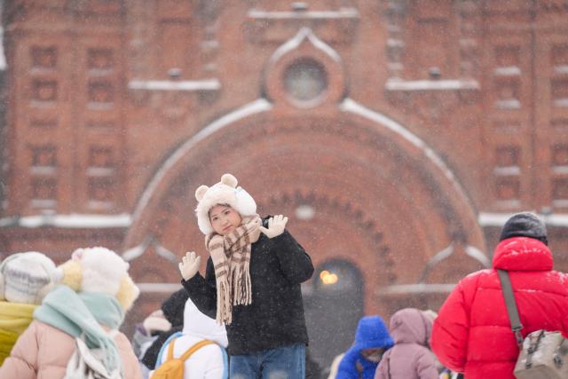 (251223) -- HARBIN, Dec. 23, 2025 (Xinhua) -- A visitor poses for photos at a square in Harbin, northeast China's Heilongjiang Province, Dec. 23, 2025. The meteorological observatory of Harbin issued a yellow alert for blizzard on Tuesday. (Xinhua/Wang Jianwei)