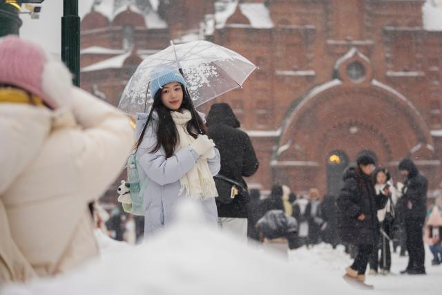 (251223) -- HARBIN, Dec. 23, 2025 (Xinhua) -- A women poses for photos at a square in Harbin, northeast China's Heilongjiang Province, Dec. 23, 2025. The meteorological observatory of Harbin issued a yellow alert for blizzard on Tuesday. (Xinhua/Wang Jianwei)