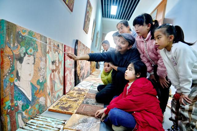 (251223) -- WUYISHAN, Dec. 23, 2025 (Xinhua) -- An artist communicates with children on rock pigment paintings in Wuyishan City, southeast China's Fujian Province, Dec. 20, 2025. Wuyishan boasts a wide range of colorful rock and soil, which serve as a natural palette for painting, giving rise to the distinctive Wuyi rock pigment art. Integrating modern artistic elements and techniques into tradition, Wuyi rock pigment painting is gradually becoming a unique cultural feature of Wuyishan. (Photo by Chen Ying/Xinhua)