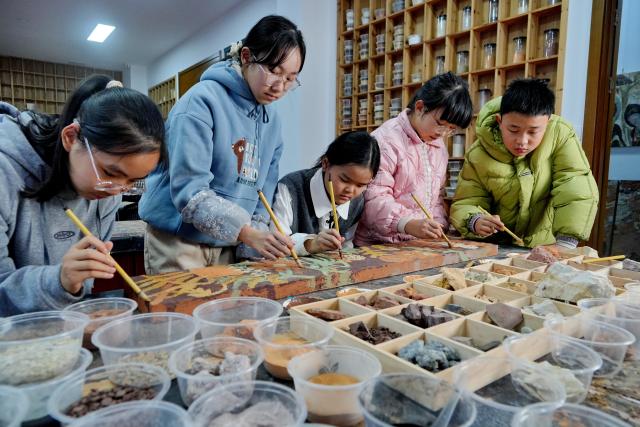 (251223) -- WUYISHAN, Dec. 23, 2025 (Xinhua) -- Children work on a piece of rock pigment painting in Wuyishan City, southeast China's Fujian Province, Dec. 20, 2025. Wuyishan boasts a wide range of colorful rock and soil, which serve as a natural palette for painting, giving rise to the distinctive Wuyi rock pigment art. Integrating modern artistic elements and techniques into tradition, Wuyi rock pigment painting is gradually becoming a unique cultural feature of Wuyishan. (Photo by Chen Ying/Xinhua)