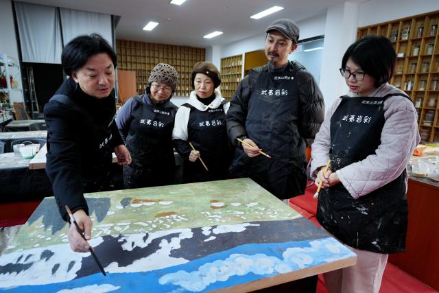 (251223) -- WUYISHAN, Dec. 23, 2025 (Xinhua) -- Artists communicate on a piece of rock pigment painting in Wuyishan City, southeast China's Fujian Province, Dec. 21, 2025. Wuyishan boasts a wide range of colorful rock and soil, which serve as a natural palette for painting, giving rise to the distinctive Wuyi rock pigment art. Integrating modern artistic elements and techniques into tradition, Wuyi rock pigment painting is gradually becoming a unique cultural feature of Wuyishan. (Photo by Chen Ying/Xinhua)