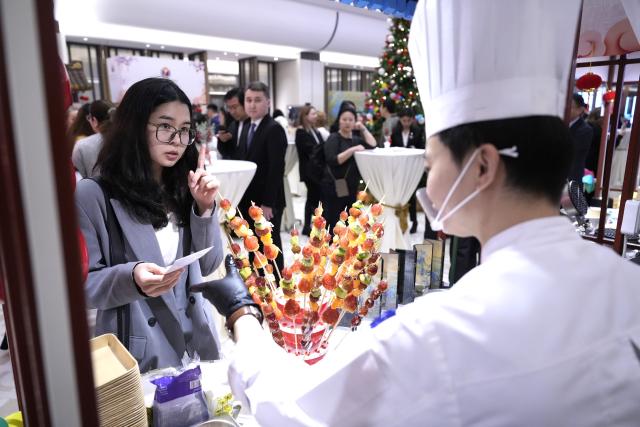 (251224) -- ASTANA, Dec. 24, 2025 (Xinhua) -- Local residents taste candied haws during the Chinese Food Festival held in Astana, Kazakhstan, Dec. 24, 2025. The Chinese Food Festival was held on Wednesday in Astana, the capital of Kazakhstan. (Photo by Kalizhan Ospanov/Xinhua)