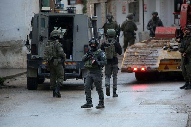 (251224) -- NABLUS, Dec. 24, 2025 (Xinhua) -- Members of Israeli forces stand guard as an Israeli bulldozer demolishes a house in the town of Bizzariya, northwest of Nablus in the West Bank, on Dec. 24, 2025. (Photo by Nidal Eshtayeh/Xinhua)