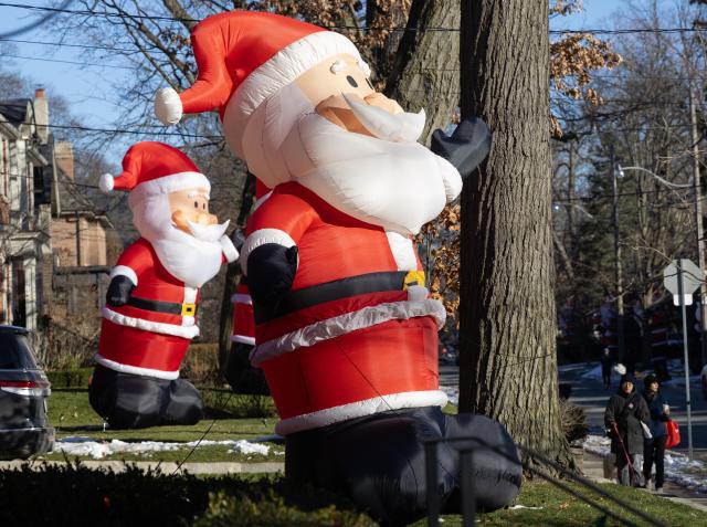 (251225) -- TORONTO, Dec. 25, 2025 (Xinhua) -- People walk past giant-sized inflatable Santa Clauses on a street in Toronto, Canada, on Dec. 24, 2025. (Photo by Zou Zheng/Xinhua)