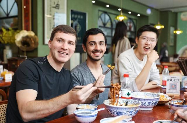 (251225) -- SHANGHAI, Dec. 25, 2025 (Xinhua) -- This photo taken in April of 2025 shows a tour guide with his tourists tasting Shanghai-style scallion oil noodles at a restaurant in Shanghai, east China. As China's latest chapter of inbound tourism begins to take shape, there are a loosely connected group of people who do not fit neatly into media narratives or influencer culture. They are present in everyday encounters, helping visitors bridge the gap between assumption and experience. In China's media and academic cultural communication circles, people have begun calling them "cultural ferrymen."
     Some are Chinese professionals who have turned away from conventional tourism; others are foreigners who have built their lives in China and now find themselves translating it. Together, they are reshaping how international visitors experience the country -- not as a spectacle, but as a lived reality. (Xinhua)