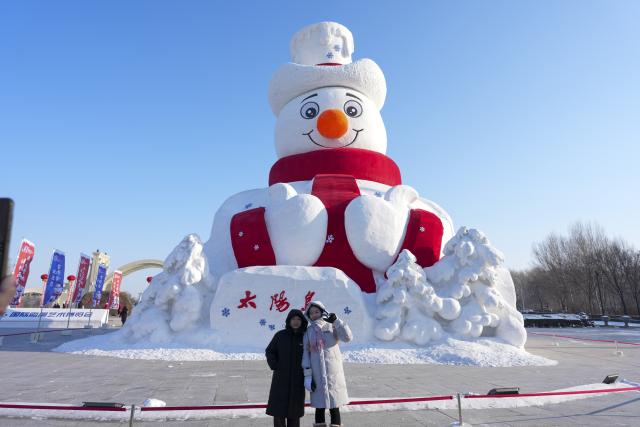 (251227) -- HARBIN, Dec. 27, 2025 (Xinhua) -- People pose for photos with "Mr. Snowman" at the entrance of the venue of the 38th Sun Island International Snow Sculpture Art Expo in Harbin, northeast China's Heilongjiang Province, Dec. 26, 2025.  "Mr. Snowman" is an iconic snow sculpture landscape of this expo. The 38th Sun Island International Snow Sculpture Art Expo opened here for trial on Saturday, with an exhibition area of 1.5 million square meters and a snow-using volume of 120,000 cubic meters. (Xinhua/Wang Song)