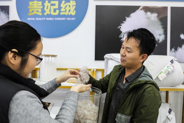 (251227) -- NANNING, Dec. 27, 2025 (Xinhua) -- This photo taken on Dec. 18, 2025 shows a staff member (R) introducing down product to a customer at a down company in Qiaoxu Town, Gangnan District of Guigang City, south China's Guangxi Zhuang Autonomous Region. Gangnan District in Guigang City of Guangxi is called "Home of down industry in China". Starting from the 1980s, the local down industry now mainly gathers in Qiaoxu Town, which after over 40 years of development, has formed a complete industrial chain covering primary feather selecting and processing, washed feather and down processing and down products making. Nowadays, there are 170 relative companies in Gangnan District, producing a total volume of feather and down of about 90,000 tonnes a year. (Xinhua/Cao Yiming)