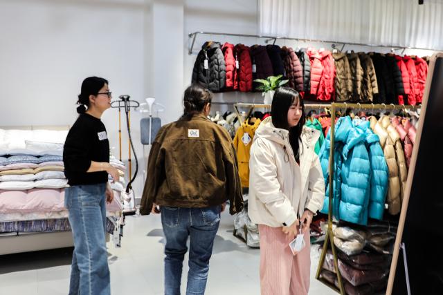 (251227) -- NANNING, Dec. 27, 2025 (Xinhua) -- This photo taken on Dec. 18, 2025 shows customers selecting down jackets in Qiaoxu Town, Gangnan District of Guigang City, south China's Guangxi Zhuang Autonomous Region. Gangnan District in Guigang City of Guangxi is called "Home of down industry in China". Starting from the 1980s, the local down industry now mainly gathers in Qiaoxu Town, which after over 40 years of development, has formed a complete industrial chain covering primary feather selecting and processing, washed feather and down processing and down products making. Nowadays, there are 170 relative companies in Gangnan District, producing a total volume of feather and down of about 90,000 tonnes a year. (Xinhua/Cao Yiming)