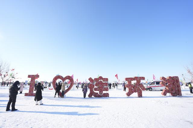 (251227) -- DAQING, Dec. 27, 2025 (Xinhua) -- Tourists pose for photos during a winter fishing event of a Nadam fair in Mongolian Autonomous County of Dorbod, Daqing City, northeast China's Heilongjiang Province, Dec. 27, 2025. An ice and snow Nadam fair featuring winter fishing kicked off here on Saturday. The integrated development fishery, and cultural and tourism industry in Dorbod has not only boosted tourism market, but also increased the income of local fishermen. (Xinhua/Wang Song)