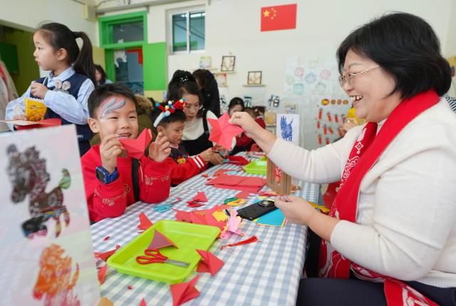 (251227) -- YINCHUAN, Dec. 27, 2025 (Xinhua) -- Children make paper-cutting works under the guidance of a paper-cutting artist at a kindergarten in Yinchuan, northwest China's Ningxia Hui Autonomous Region, Dec. 27, 2025. As the New Year approaches, a kindergarten in Yinchuan City held an activity and invited inheritors of intangible cultural heritage to promote lion dance, paper-cutting making and sugar painting. (Xinhua/Wang Peng)