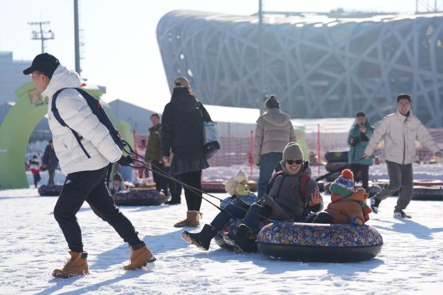 (251227) -- BEIJING, Dec. 27, 2025 (Xinhua) -- People enjoy sliding on an inflatable snow sled outside the National Stadium, also known as the Bird's Nest, in Beijing, capital of China, Dec. 27, 2025. The winter theme park of the Bird's Nest kicked off on Saturday and will run till late February 2026. The event features an ice and snow activity zone, and an outdoor fashion and leisure zone. (Xinhua/Xie Han)