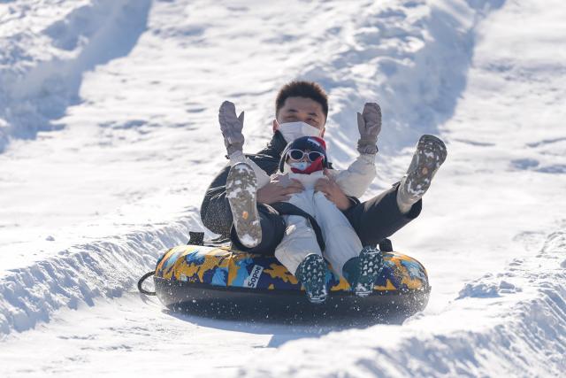 (251227) -- BEIJING, Dec. 27, 2025 (Xinhua) -- People enjoy sliding on an inflatable snow sled outside the National Stadium, also known as the Bird's Nest, in Beijing, capital of China, Dec. 27, 2025. The winter theme park of the Bird's Nest kicked off on Saturday and will run till late February 2026. The event features an ice and snow activity zone, and an outdoor fashion and leisure zone. (Xinhua/Xie Han)