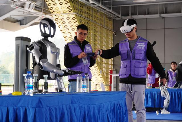 (251227) -- SHENZHEN, Dec. 27, 2025 (Xinhua) -- Contestants control a robot during a robot skills competition in Shenzhen, south China's Guangdong Province, Dec. 27, 2025. The robot skills competition kicked off here on Friday and will last till Dec. 30, 2025. Over 100 teams participate in robot application matches ranging from industrial manufacturing, healthcare to emergency rescue scenarios. (Xinhua/Wang Feng)