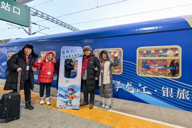 (251228) -- HARBIN, Dec. 28, 2025 (Xinhua) -- Tourists pose for photos with a tourism train at Harbin East Railway Station in Harbin, northeast China's Heilongjiang Province, Dec. 28, 2025. Train Y999/998, an ice-and-snow themed tourism loop train, started a six-day trip on Sunday. (Photo by Yuan Yong/Xinhua)