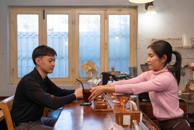 (251230) -- CHAMPASAK, Dec. 30, 2025 (Xinhua) -- A customer (L) enjoys coffee at a coffee shop in Vientiane, Laos, Dec. 22, 2025. TO GO WITH "Feature: Lao coffee's aroma goes global" (Photo by Ma Huaizhao/Xinhua)