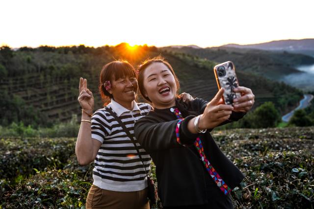 (251231) -- JINGHONG, Dec. 31, 2025 (Xinhua) -- Wei Chun (R) and her mother take a selfie at a tea plantation in Dadugang Township of Jinghong City, Xishuangbanna Dai Autonomous Prefecture, southwest China's Yunnan Province, Dec. 21, 2025. Wei Chun used to work at an international hotel in a first-tier city. In June 2024, she became an agricultural manager of a collective economy company in Dadugang Township, a role locals refer to as the "Village CEO." 
   Under her leadership, idle factory buildings and vacant land were transformed into cafes, educational spaces, and campsites, providing recreational spaces for visitors. Wei also offered free training in coffee making, tea art, and rural hospitality management, improving service quality and expanding employment opportunities for villagers.
   By 2025, Wei has helped more than 100 villagers acquire new skills and attracted nine talents returning home to start businesses here. (Xinhua/Hu Chao)
