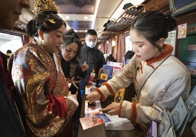 (260101) -- BEIJING, Jan. 1, 2026 (Xinhua) -- Tourists purchase commemorative envelopes and postcards on a themed train running from Tianjin North Railway Station to Beijing Railway Station, Jan. 1, 2026. The Tianjin Fantasy Express has begun a scheduled round-trip service between Tianjin North Railway Station and Beijing Railway Station since Thursday. The line features 10 distinctively themed carriages integrating art performances, cultural presentations and intangible cultural heritage experience. (Xinhua/Zhang Fan)