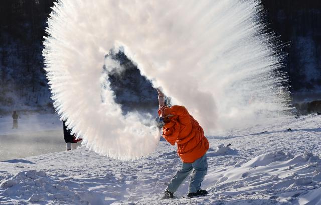 (260101) -- ARXAN, Jan. 1, 2026 (Xinhua) -- A tourist plays a "water to ice" game by splashing water into the cold air by the Halha River in the city of Arxan of Hinggan League, north China's Inner Mongolia Autonomous Region, Jan. 1, 2026. Despite Arxan's frigid winter cold, this geothermally-affected section of the Halha River never freezes, which attracts great amount of tourists in winter. (Photo by Wang Zheng/Xinhua)