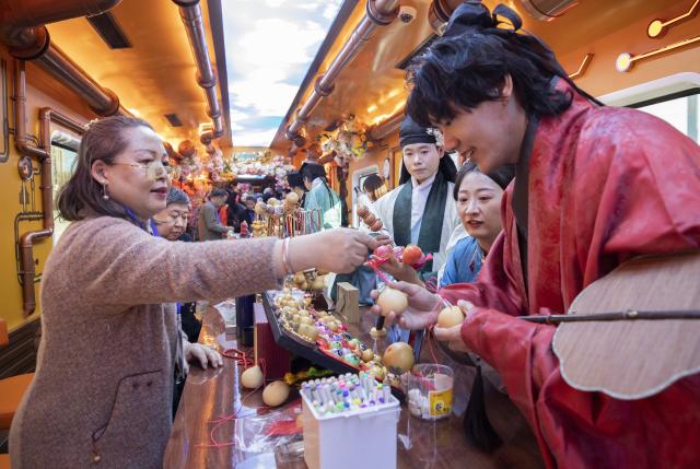 (260102) -- BEIJING, Jan. 2, 2026 (Xinhua) -- Tourists learn about intangible cultural heritage on a themed train running from Beijing Railway Station to Tianjin North Railway Station, Jan. 1, 2026. The Tianjin Fantasy Express has begun a scheduled round-trip service between Tianjin North Railway Station and Beijing Railway Station since Thursday. The line features 10 distinctively themed carriages integrating art performances, cultural presentations and intangible cultural heritage experience. (Xinhua/Zhang Fan)